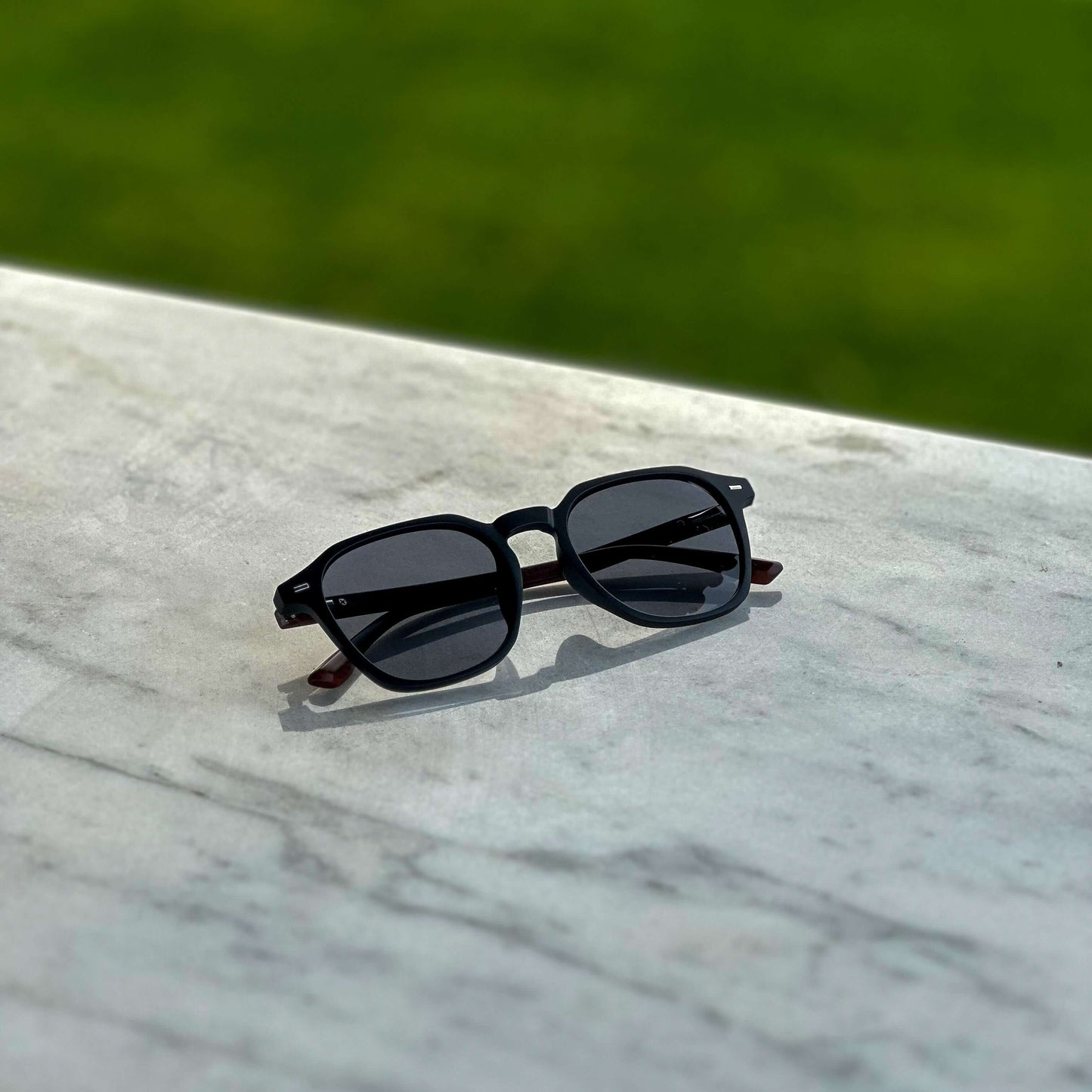 Zwarte Aero zonnebril met houtlook op luxe marmeren tafel – stijlvolle zonnebril voor de moderne man