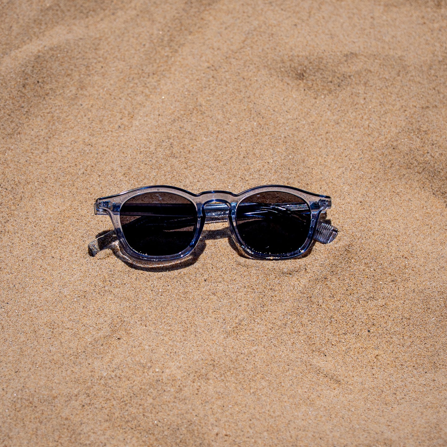 Collin blauwe zonnebril close-up in zand | opvallende kleur met UV400 bescherming
