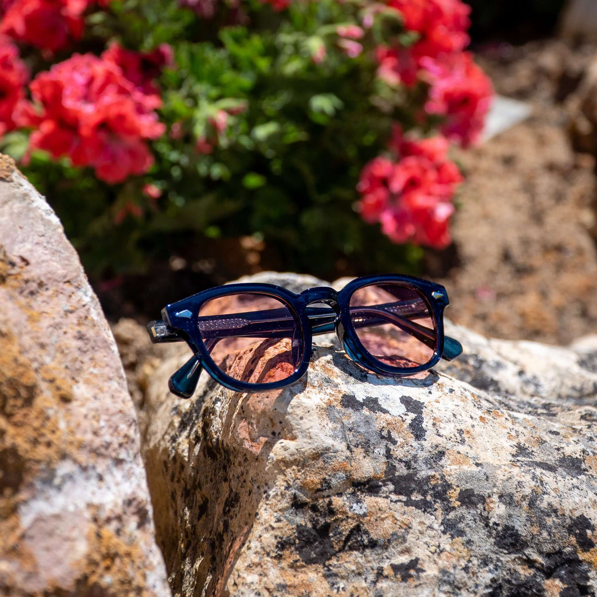 Monarch zonnebril blauw met rode glazen op steen bij de zee | retro-chique strandstijl