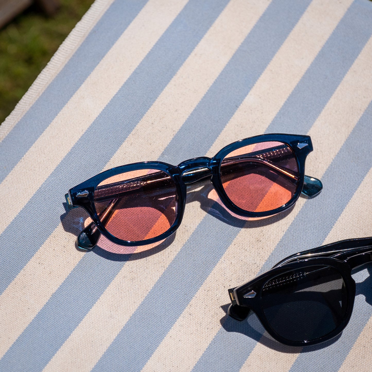 Monarch zonnebril blauw met rode glazen op luxe blauw-wit strandstoeltje | stijlvolle zomerlook