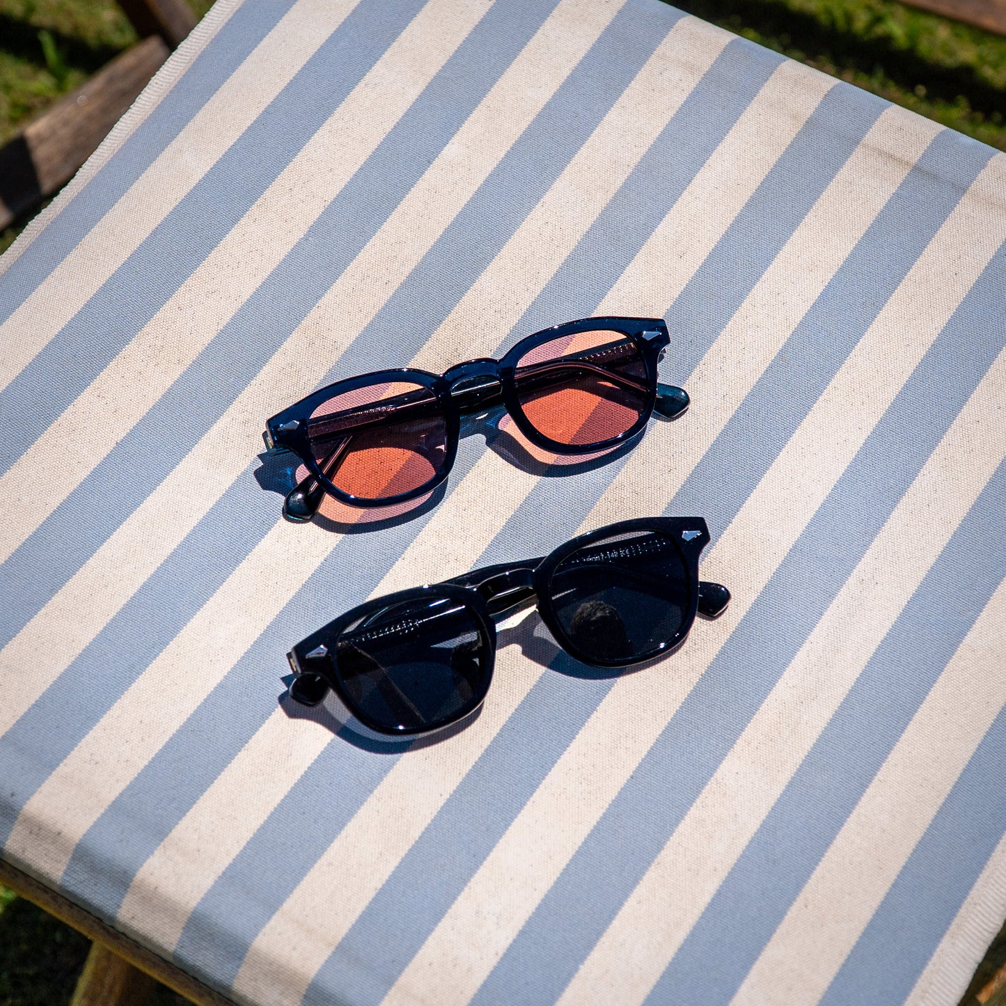 Monarch zonnebrillen zwart en blauw met rode glazen op luxe strandstoel | old money strandstijl