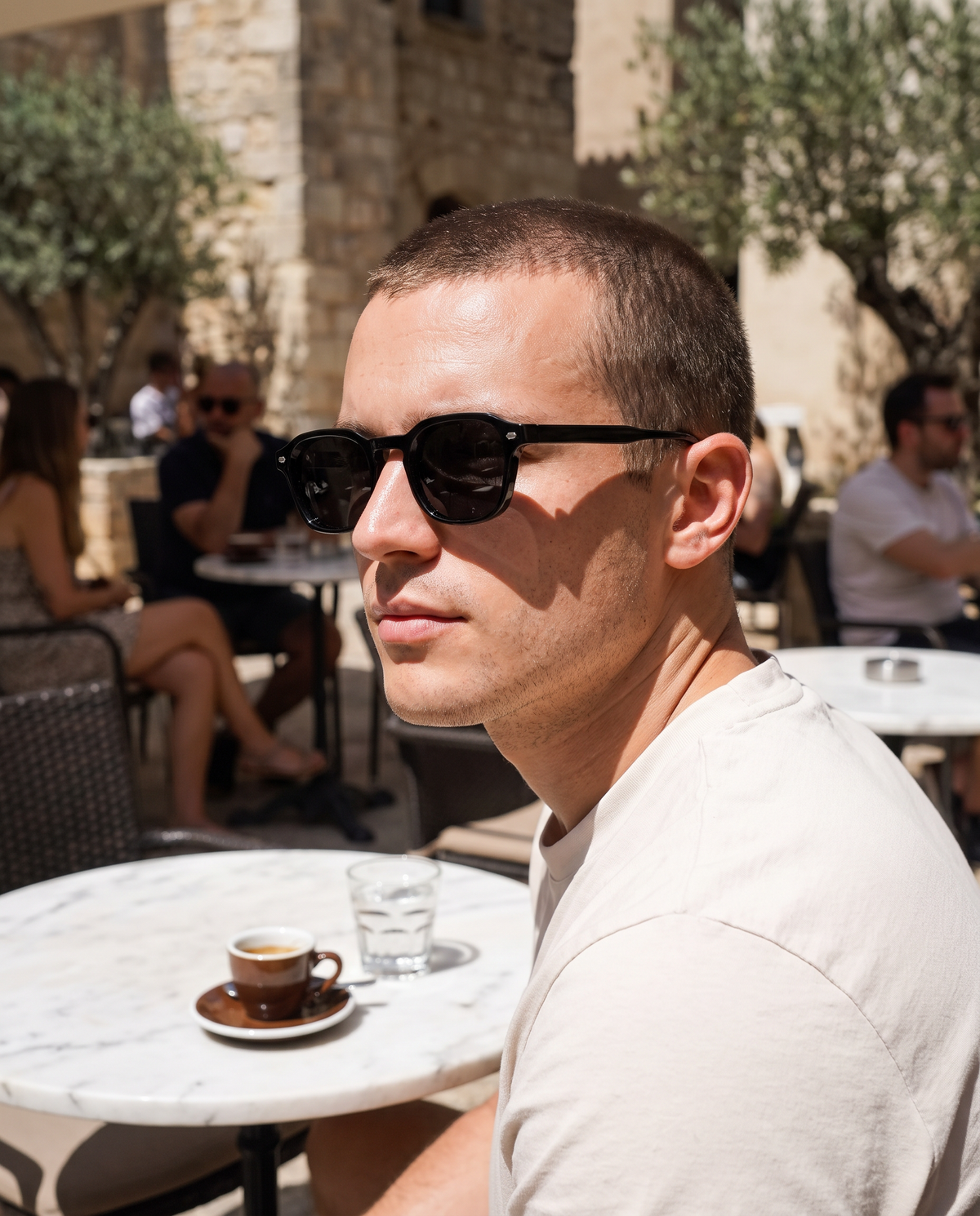 TIBOR sunglasses, black, worn on a terrace in hard midday light