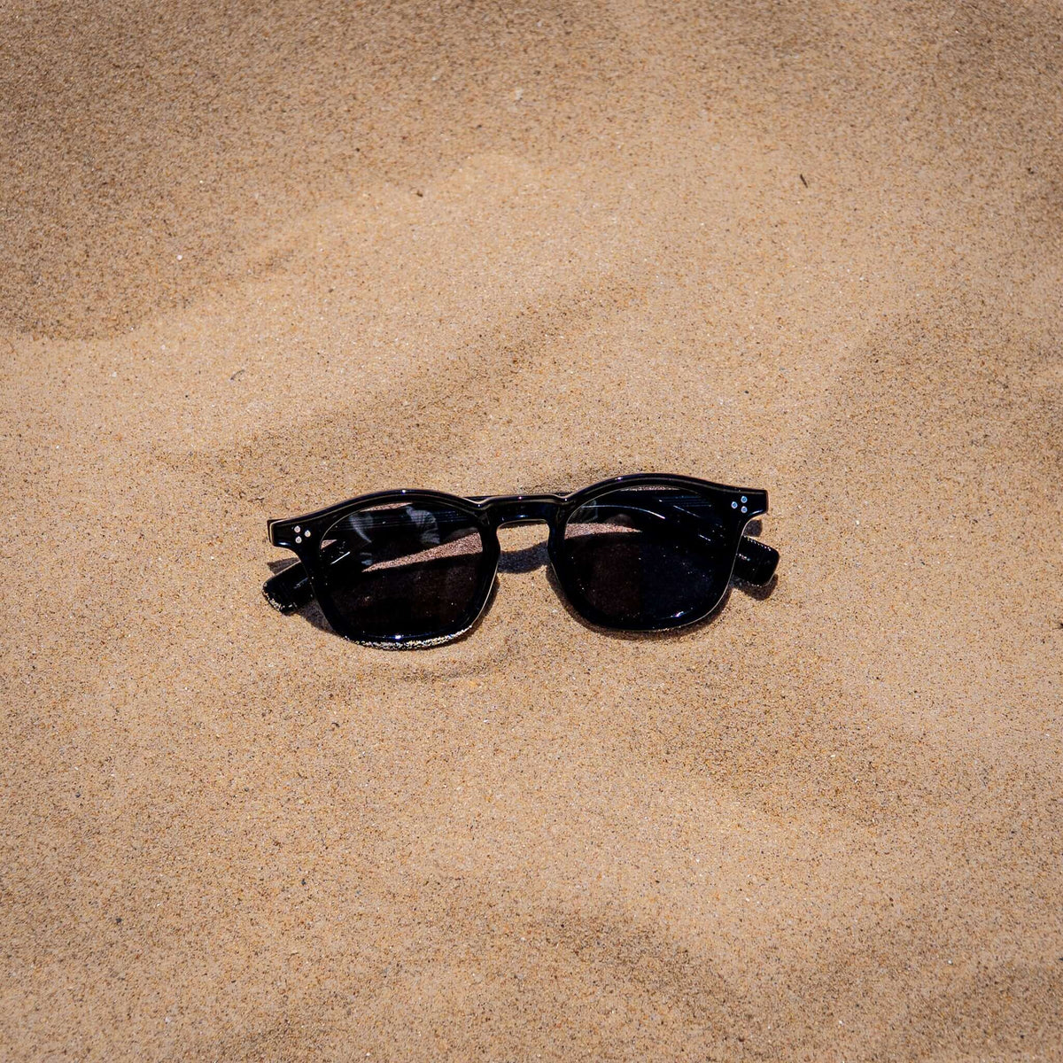 Collin zwarte zonnebril in zand close-up | klassiek unisex design
