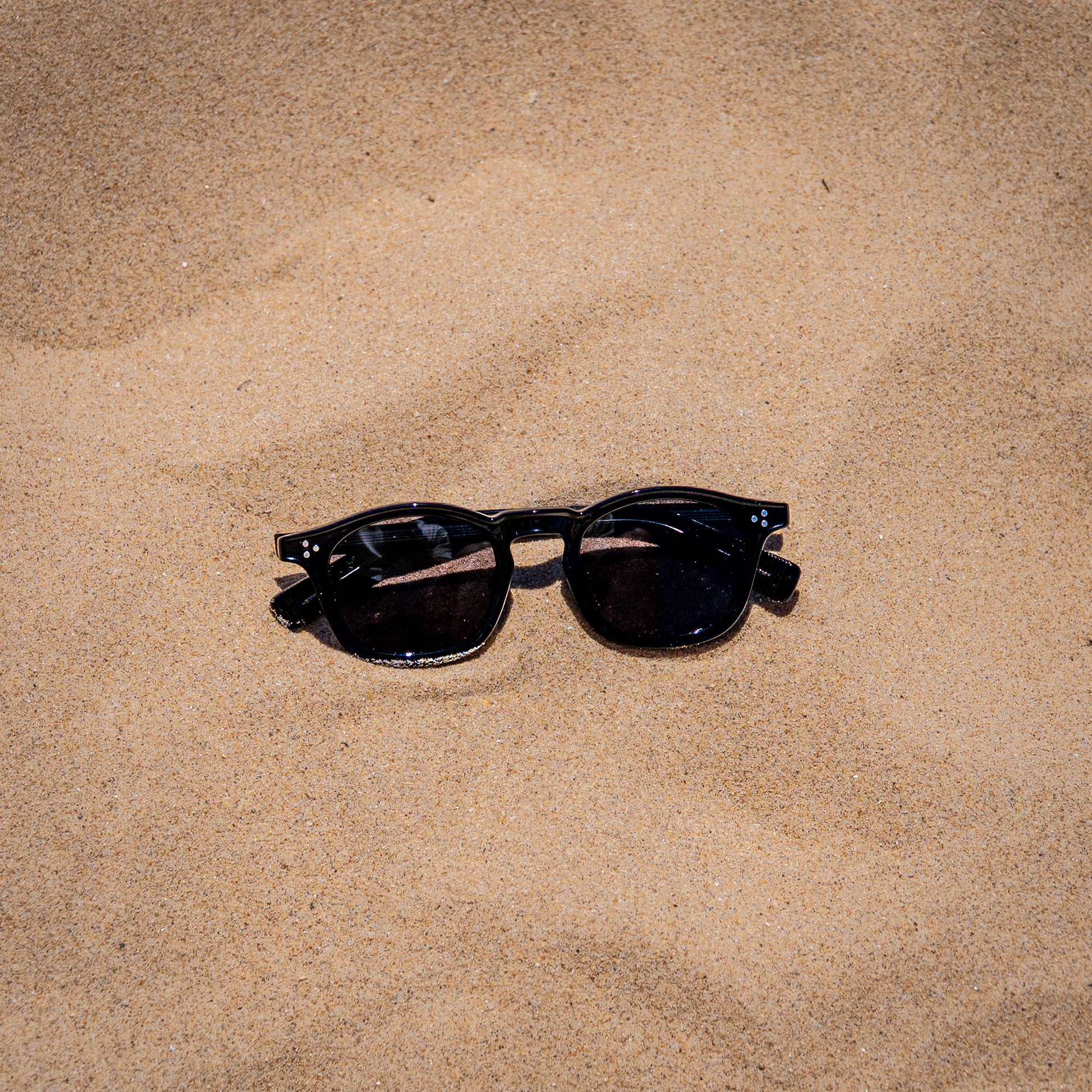 Collin zwarte zonnebril in zand close-up | klassiek unisex design