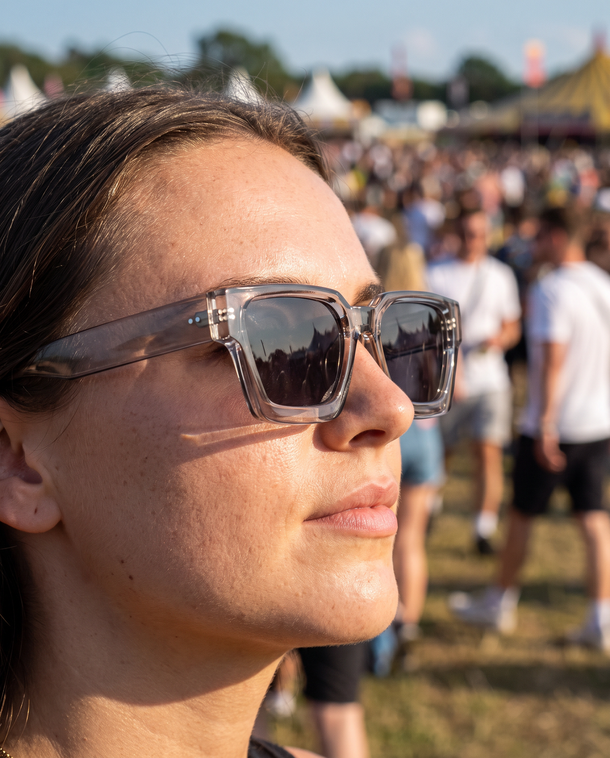 JOHN zonnebril transparant grijs gedragen op een festivalterrein in hard middaglicht