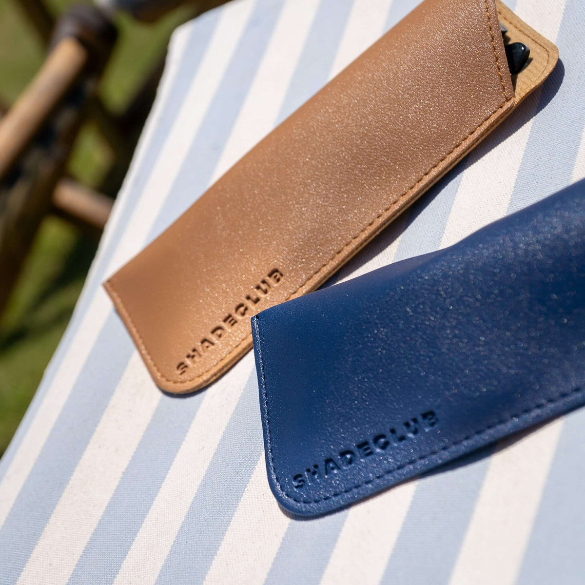 Shadeclub zonnebrillenhoesjes in navy blauw en beige op blauw-wit gestreept strandstoeltje | luxe zomeraccessoires voor stijlvolle bescherming