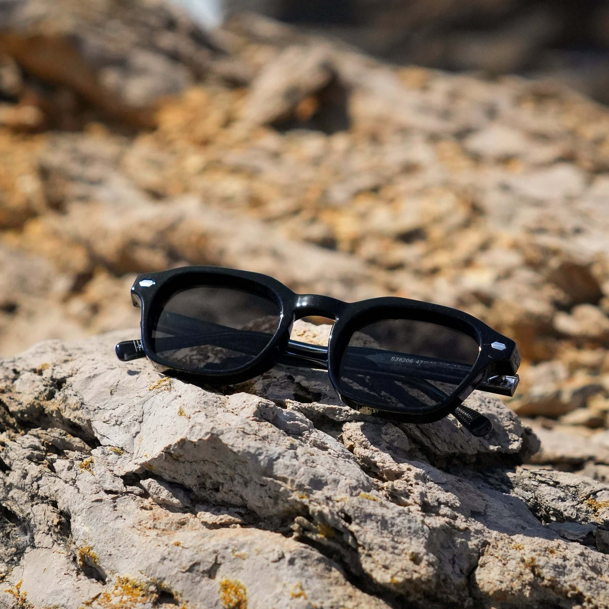TIBOR sunglasses, black, on Mediterranean coastal stones in hard sunlight